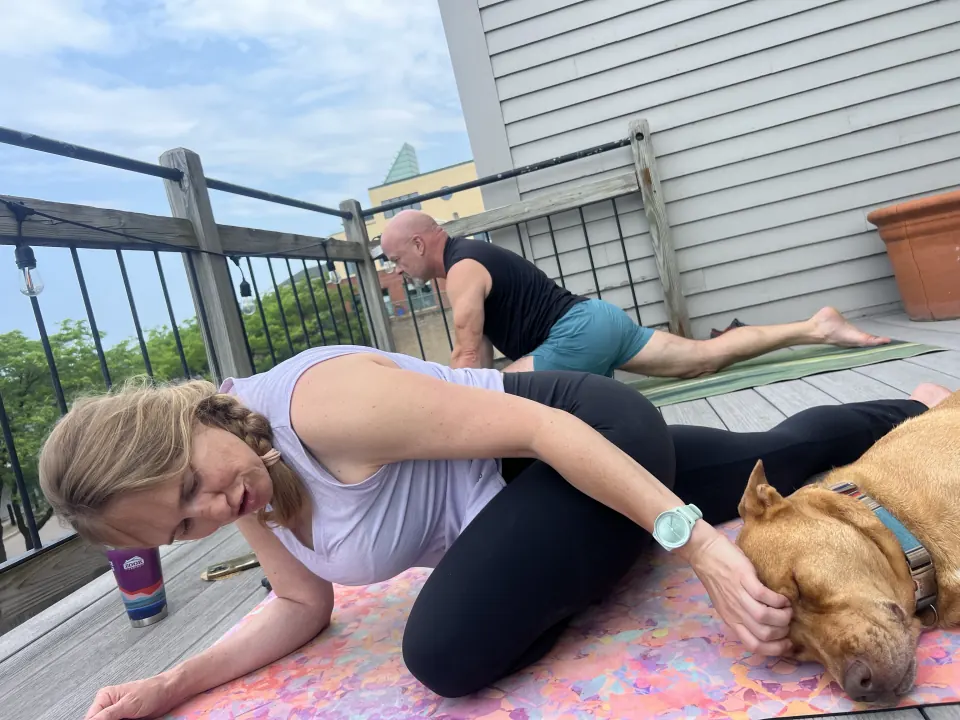 A member on her mat on a deck, one hand on a dog beside her